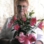 Older woman with short light hair and glasses holding a pink-flowered bouquet with a pink ribbon bow.